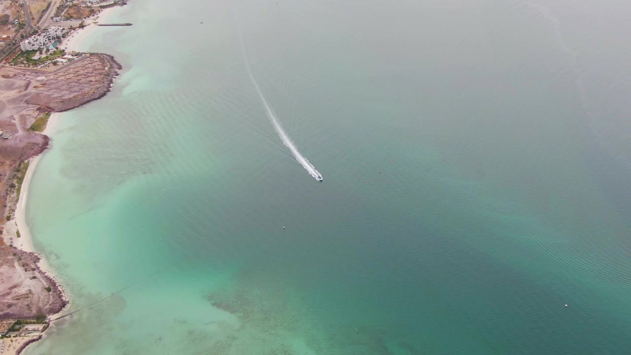 Aerial La Paz coastal frame with the shoreline compressed along the left side, the boat high over open water, and no visible people.
