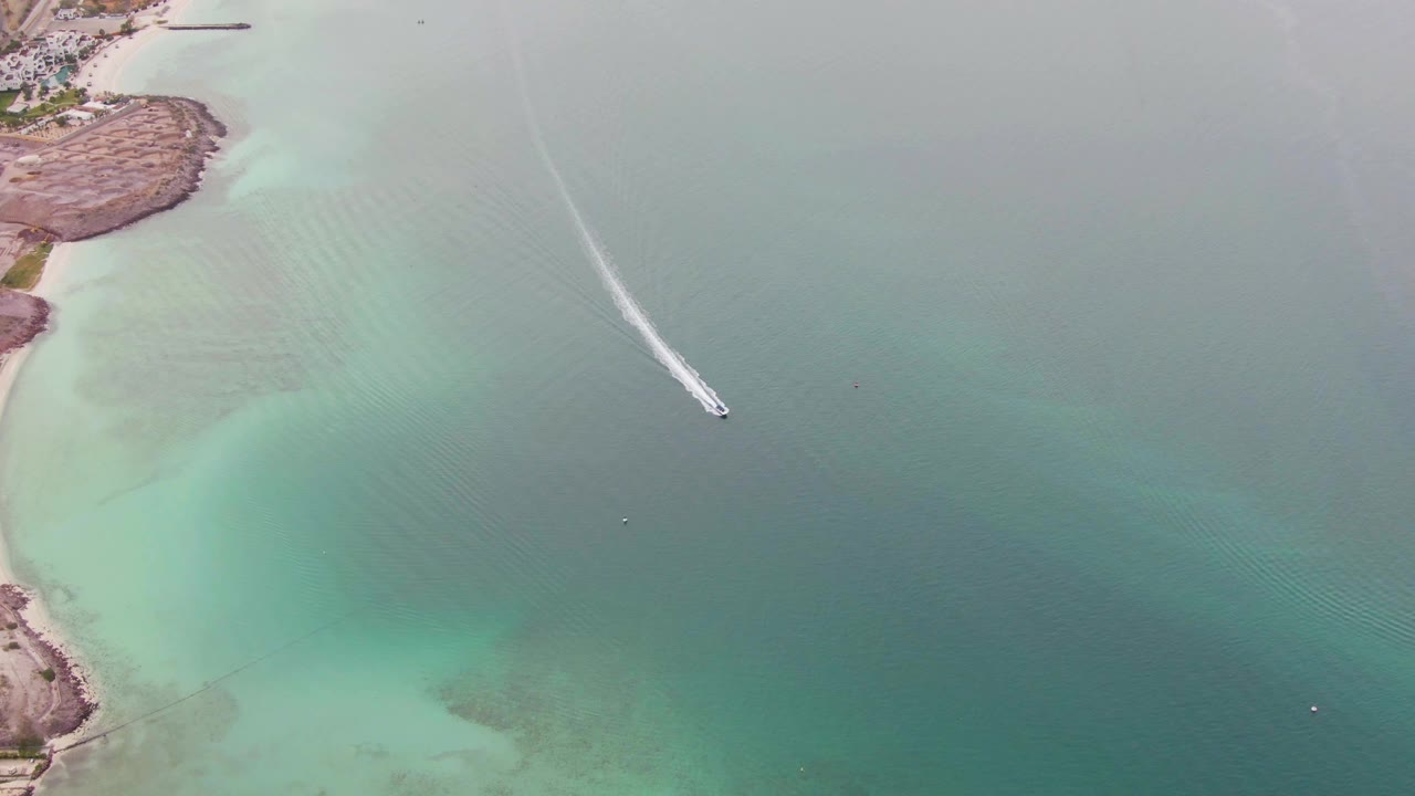 Aerial coastal water with a boat wake and pale shoreline shallows