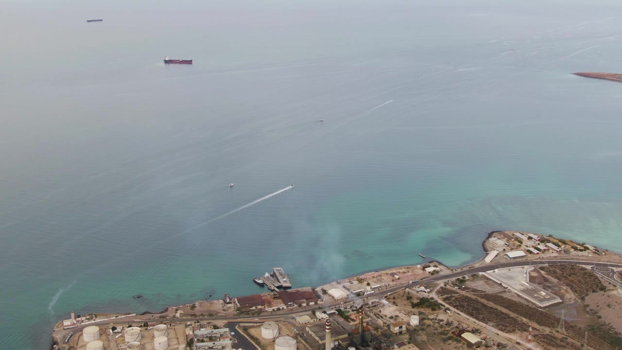 Aerial view of a speedboat wake near an industrial shoreline and distant ships.