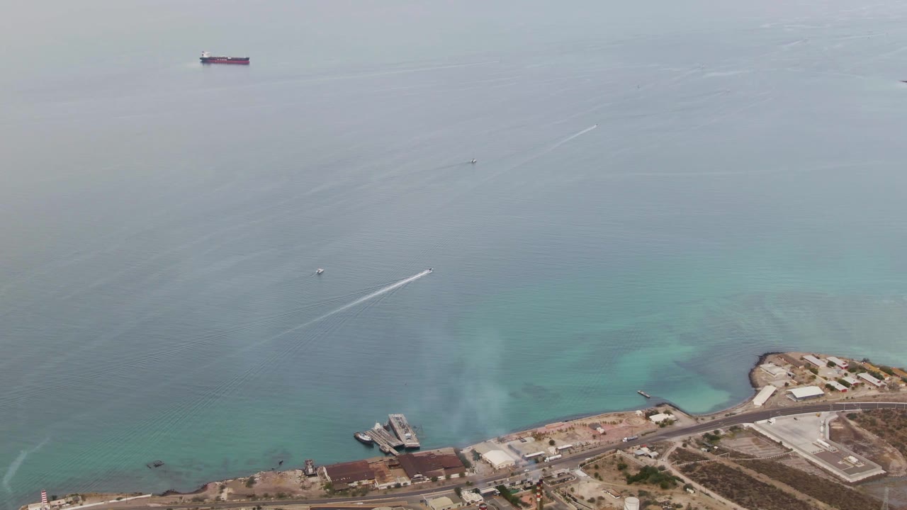 The third frame shows the speedboat and wake higher over the water, with La Paz industrial shoreline, piers, roads, and pale turquoise shallows visible below, and no visible people.