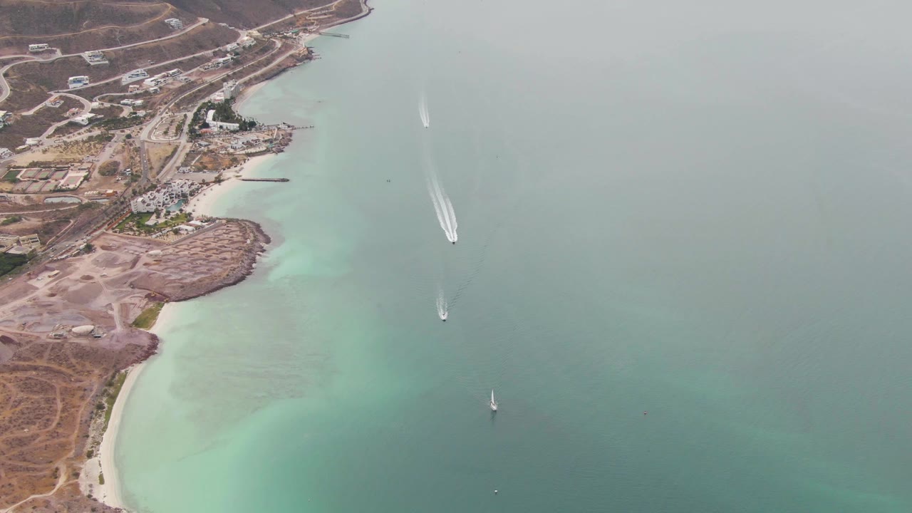 Aerial view of boats in turquoise coastal water beside a sandy shoreline.