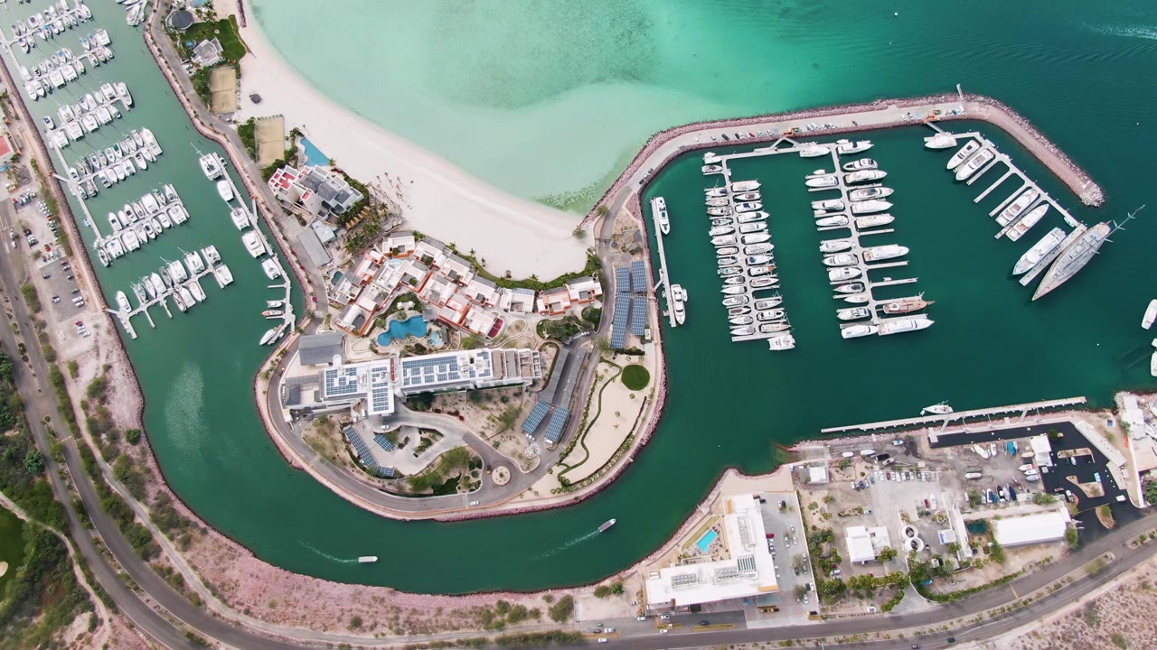 Aerial marina frame with yachts, beach, roads, and harbor water.