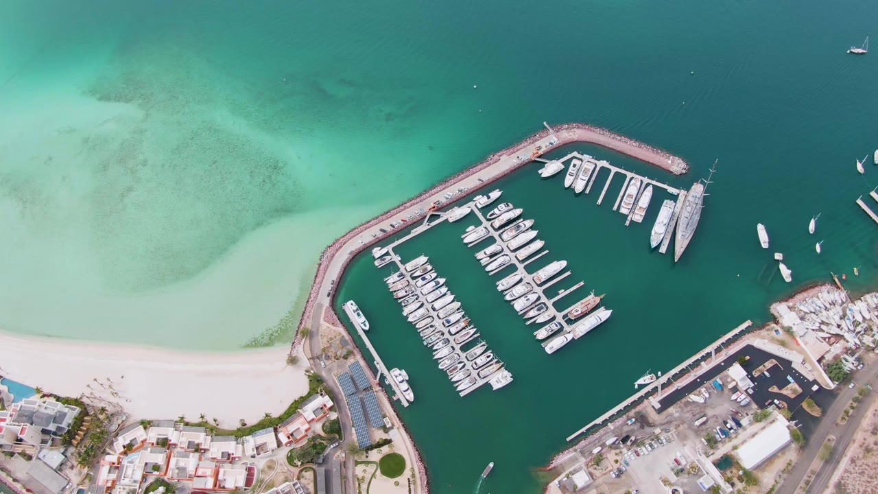 Aerial view of marina slips and pale beach beside green-blue water.