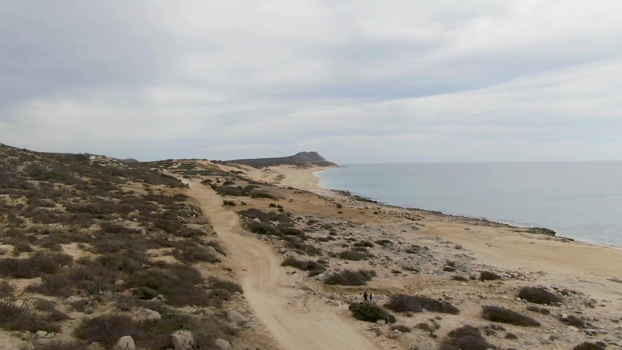 Coastal dirt road curves along scrubland above the beach.