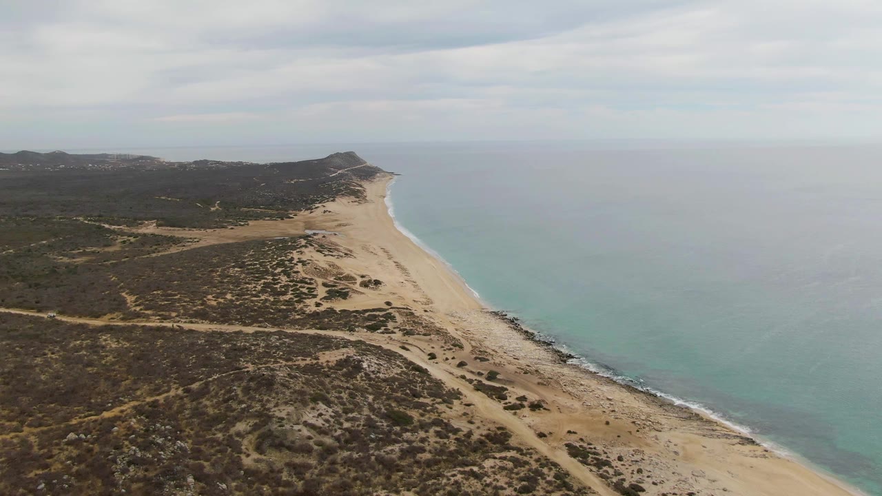 Aerial view of sandy beach, dunes, scrub vegetation, and turquoise ocean