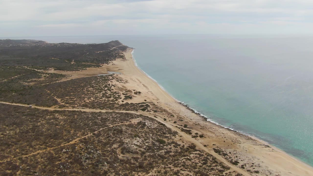Drone view of curving beach, pale surf line, and arid coastal scrub