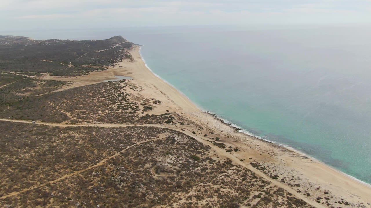 Aerial view of sandy beach, coastal dunes, and turquoise ocean.