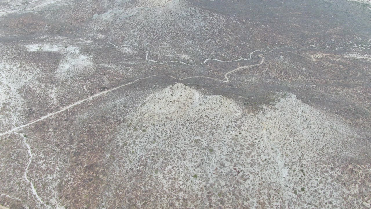 Aerial view of gray-brown hills near Punta Gorda Beach, Baja California Sur, with thin snow cover, a winding road, and no visible people.