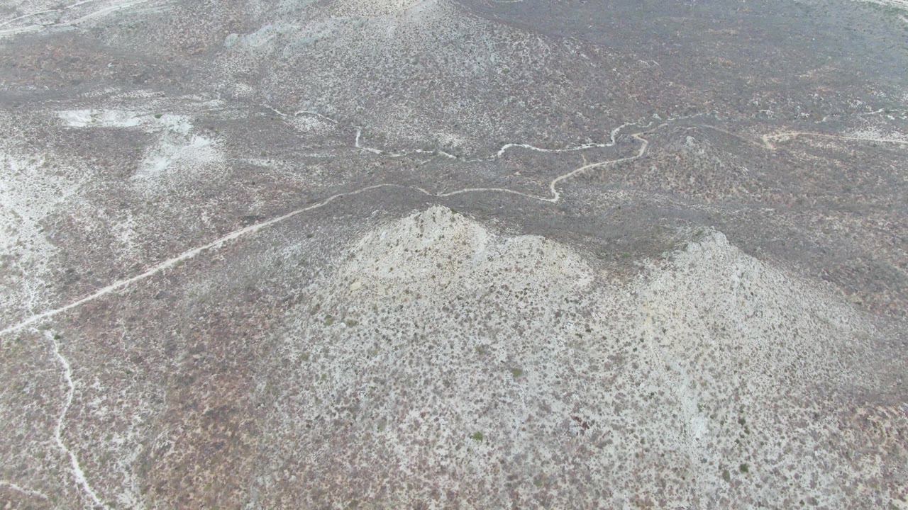 Snowfall softens an elevated view of ridge terrain near Punta Gorda Beach, Baja California Sur, where a pale road bends across the midground and no visible people appear.