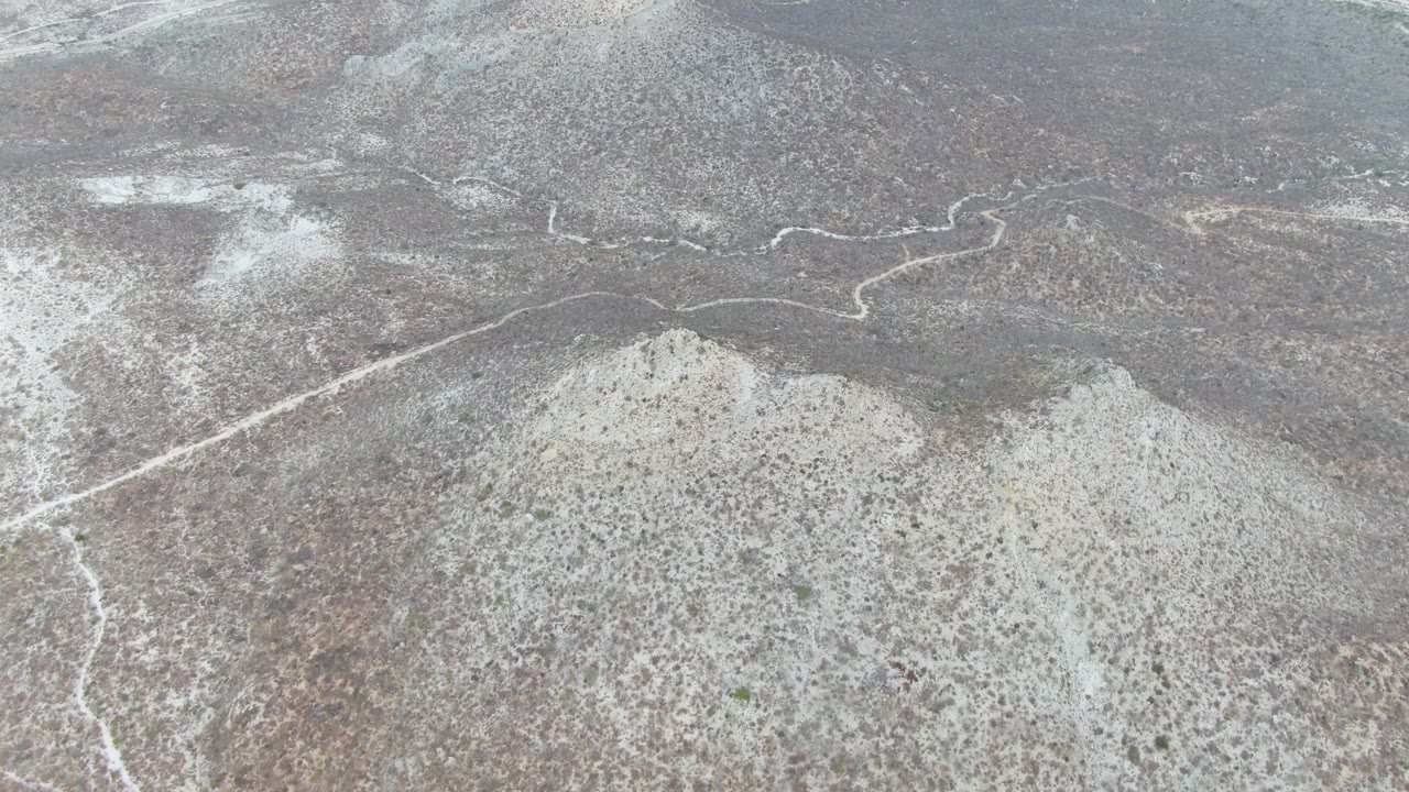 Patchy white snow covers scrubby hills near Punta Gorda Beach, Baja California Sur, with a winding road visible across the slope and no visible people.
