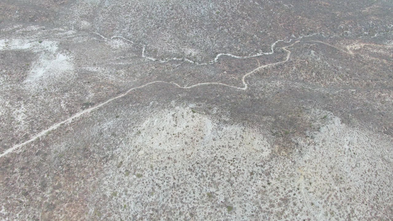 Overhead Punta Gorda Beach desert view with the road bending across the upper frame and dust hanging over gray scrubland, with no visible people.