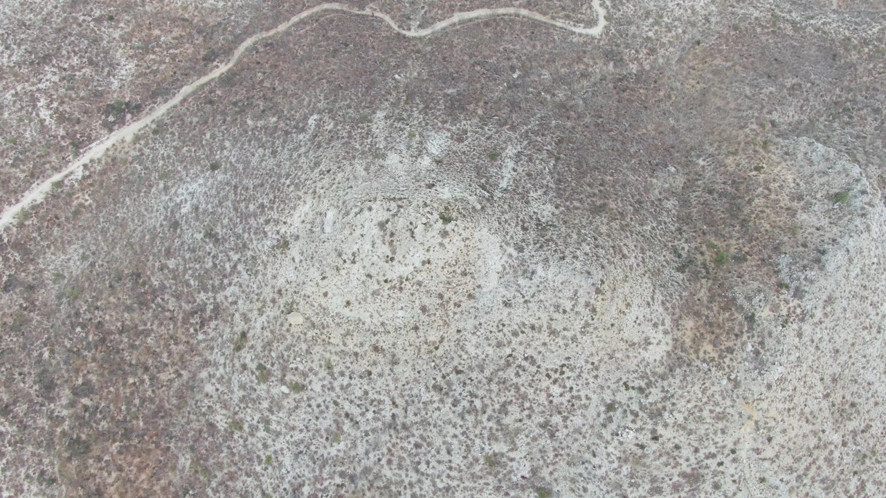 Overhead view at Punta Gorda Beach, Baja California Sur, showing a pale dry playa below brown desert scrub with a winding dirt road near the top edge and no visible people.