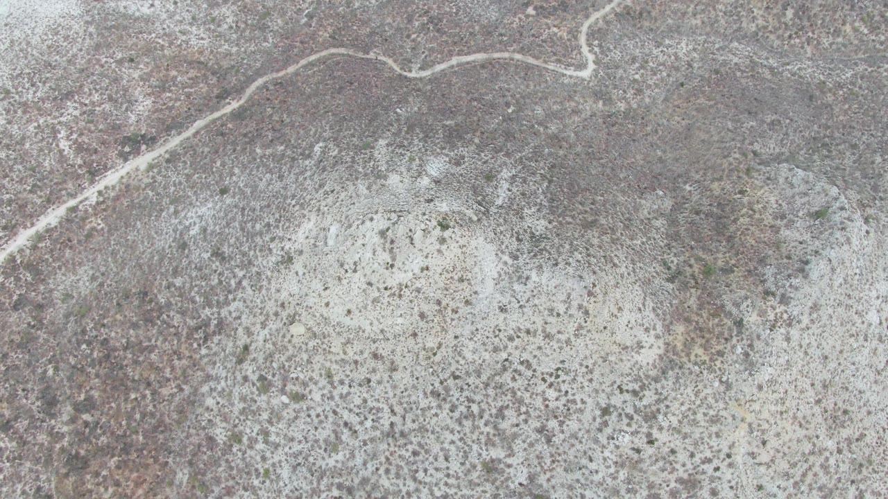 Diagonal dirt road and mottled desert ground seen from above.