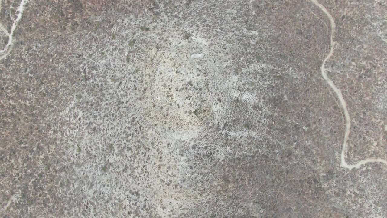 Overhead frame from Punta Gorda Beach, Baja California Sur showing pale foamy water texture spread across dry gray-brown ground with no visible people.