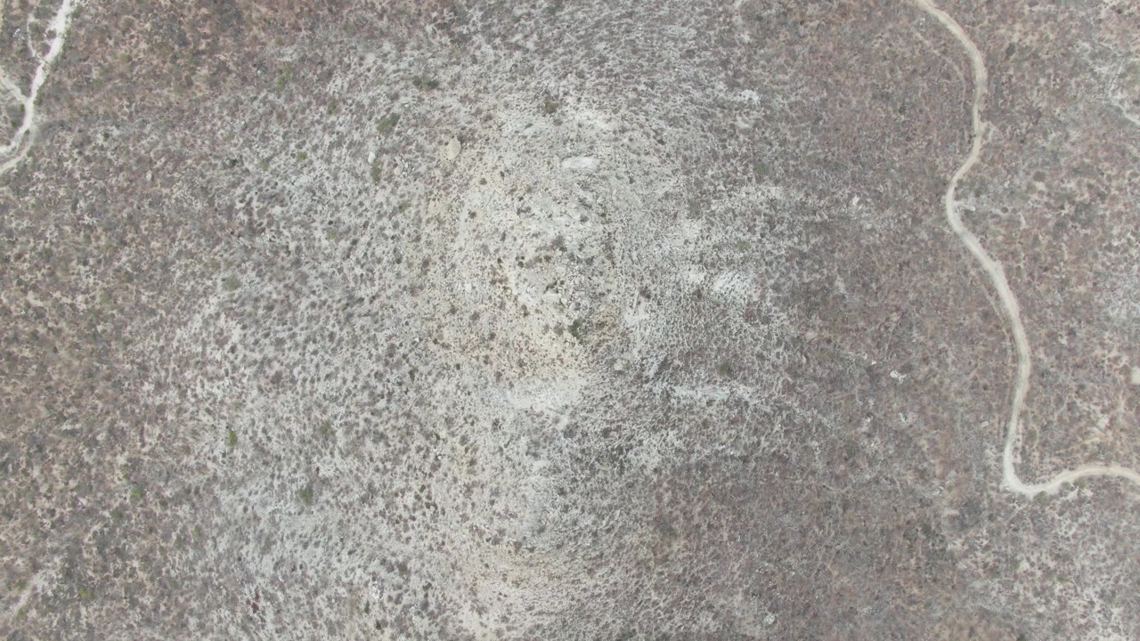 Aerial frame at Punta Gorda Beach, Baja California Sur showing a narrow pale winding flow line beside mottled dry terrain and no visible people.