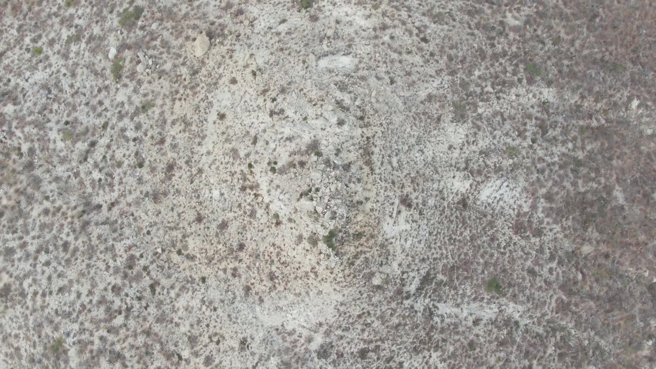 Overhead Punta Gorda Beach frame with gray rocky ground, small pale stone areas, darker mottled texture, and no visible people.