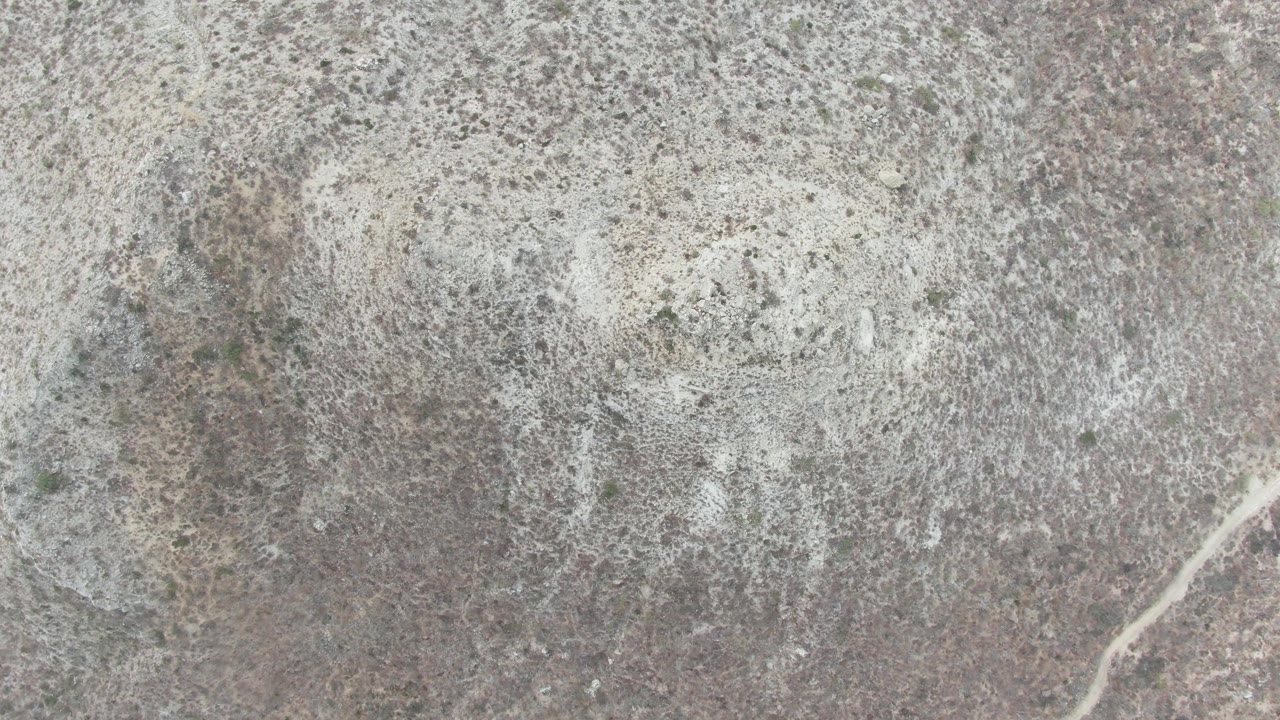 Top-down view of rocky arid ground at Punta Gorda Beach BCS, Mexico, with sparse vegetation, a faint diagonal dirt road, and no visible people.