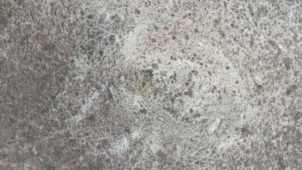 Top-down sandy terrain with mottled brush and rough rocky patches.