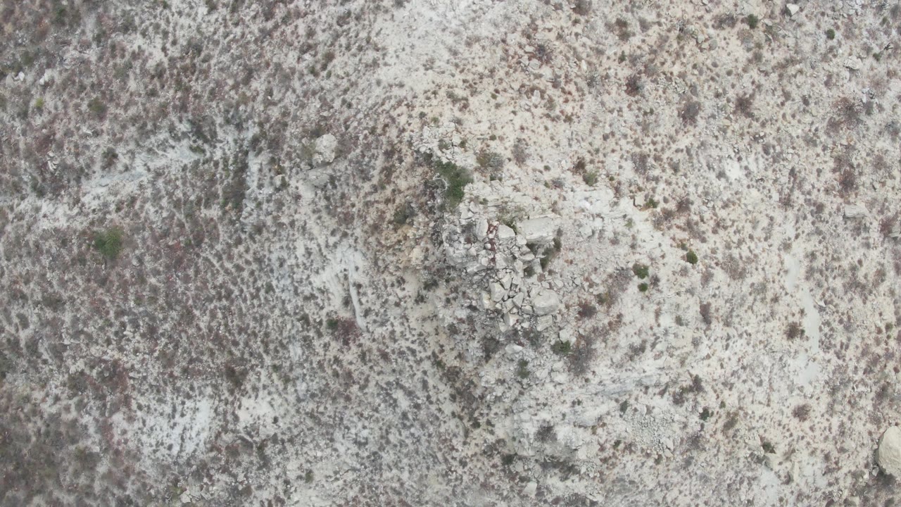 Overhead aerial frame of Punta Gorda Beach desert terrain with beige soil, scattered brush, central rock clusters, and no visible people.