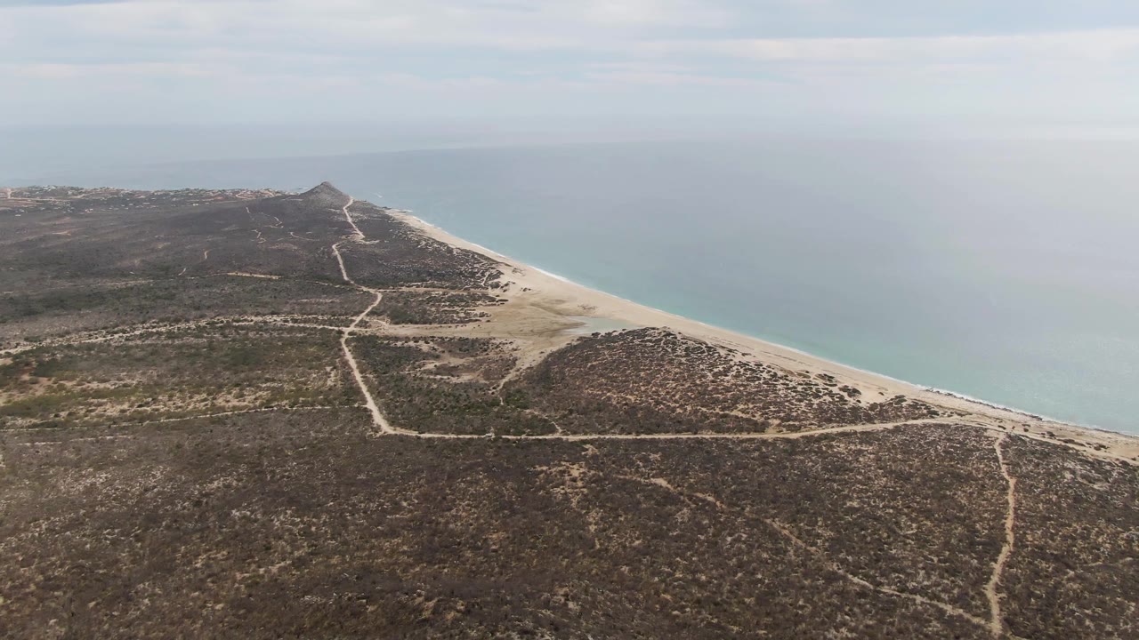 At 0:02, Punta Gorda Beach BCS appears from above with intersecting dirt paths in the foreground, a narrow sand strip, calm ocean, and no visible people.