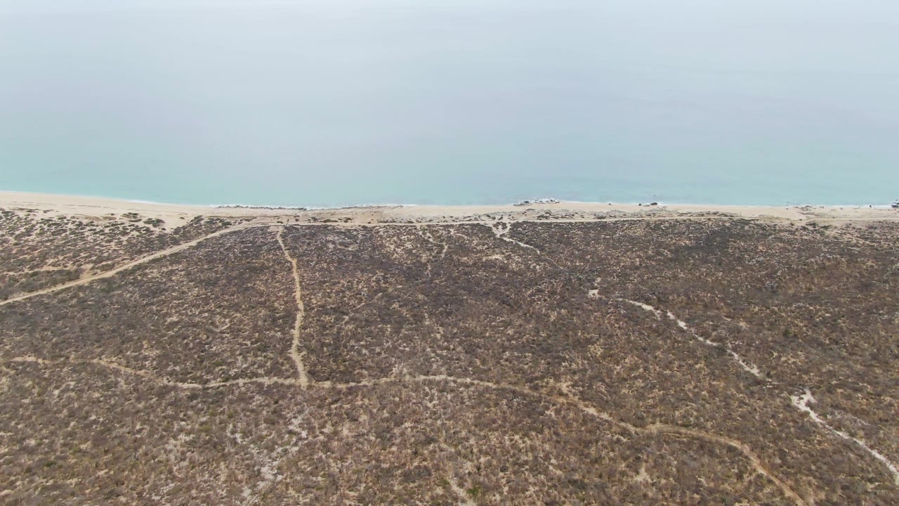 Wide drone view of dune tracks leading toward a beach and ocean.