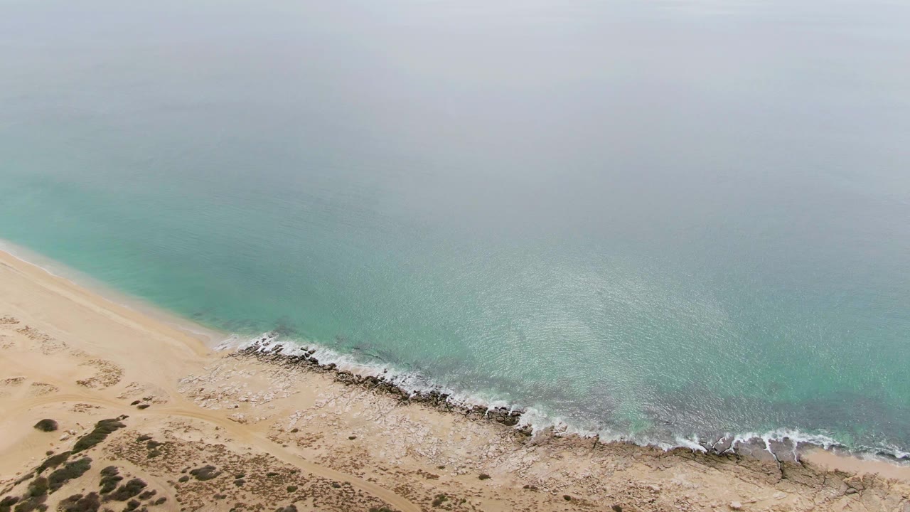 Aerial view of turquoise water meeting a sandy rocky beach