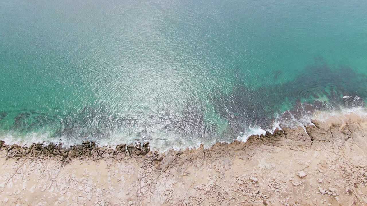 Turquoise ocean and foamy wave along rocky sandy coast