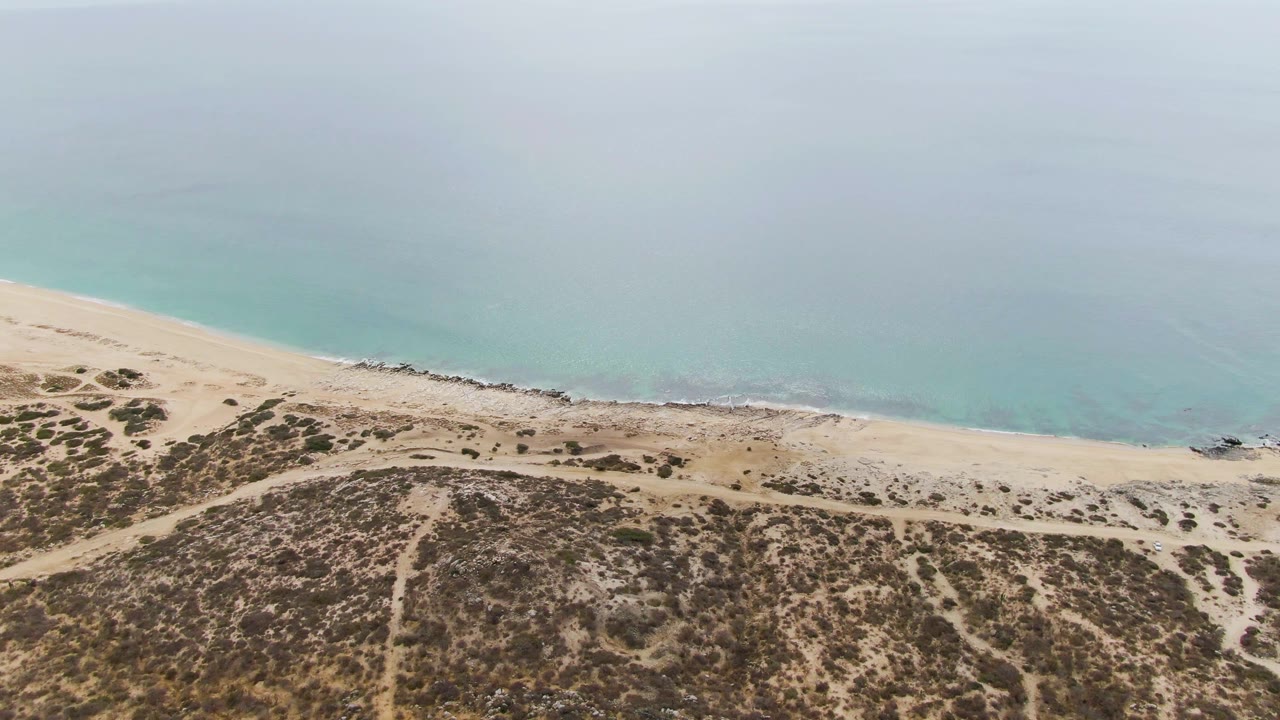 Aerial view of sandy dunes beside turquoise ocean shoreline.