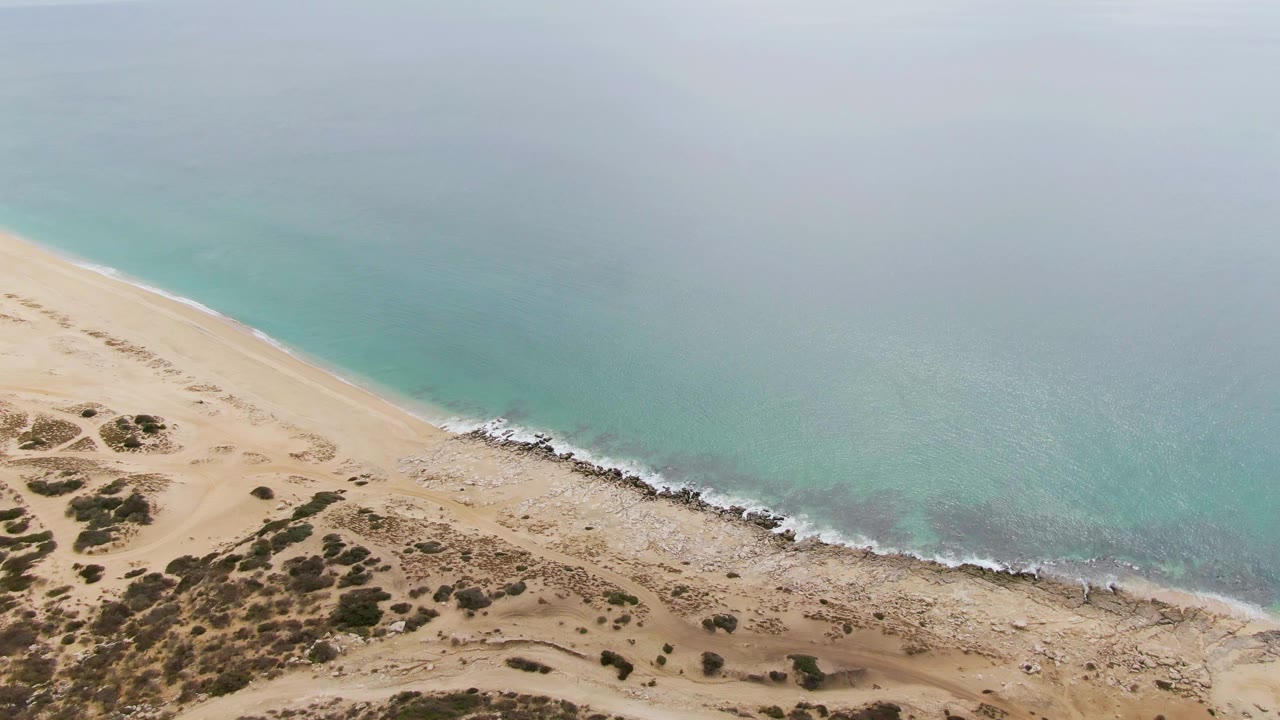 At 0:02, the aerial composition shows more open turquoise water above the Punta Gorda Beach shoreline, with rocks tracing the waterline and dune shrubs below, with no visible people.