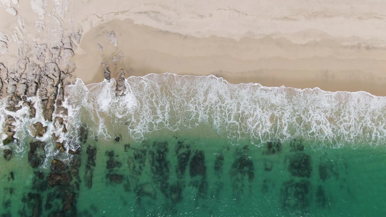 Foamy wave breaking over dark rocks in turquoise water