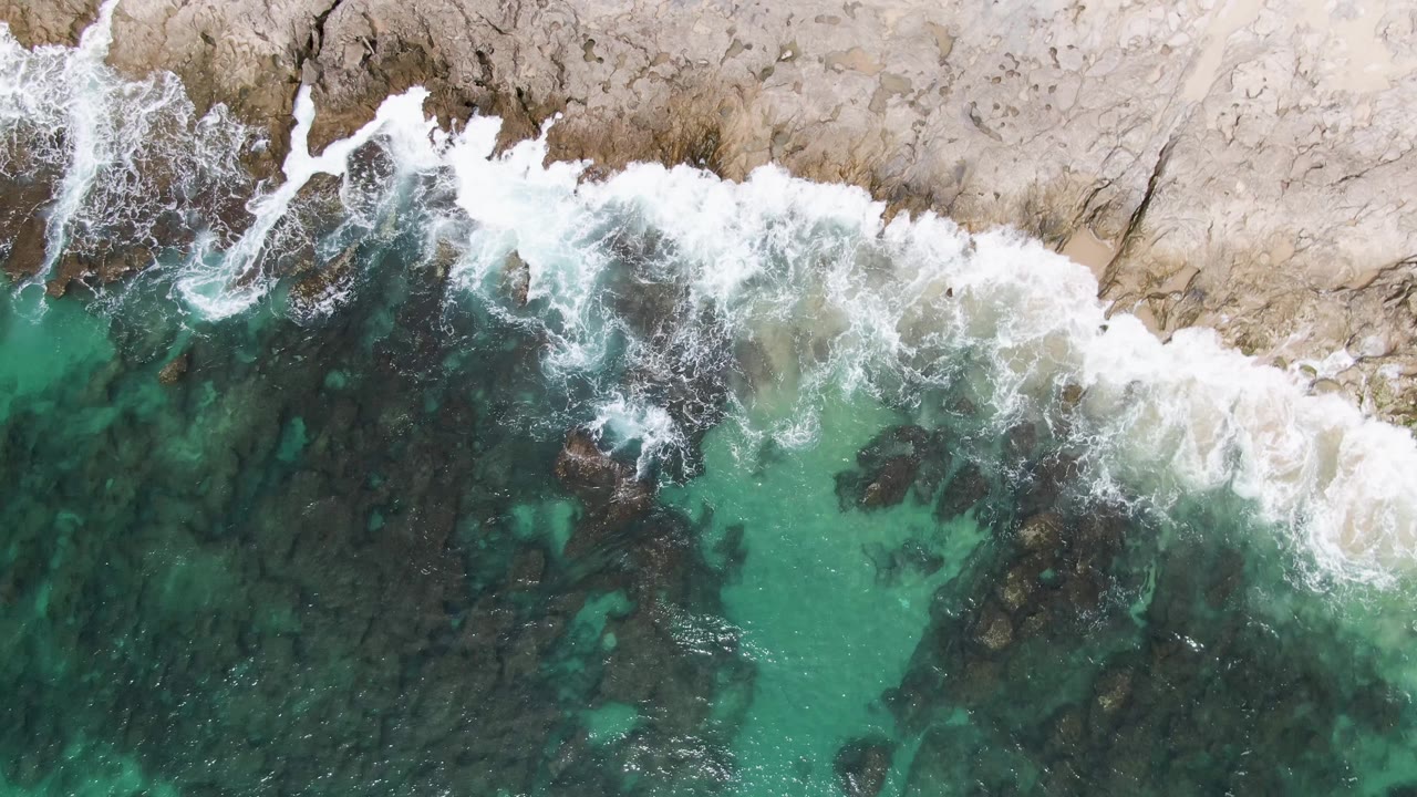 Overhead turquoise surf hitting pale rocky shoreline.