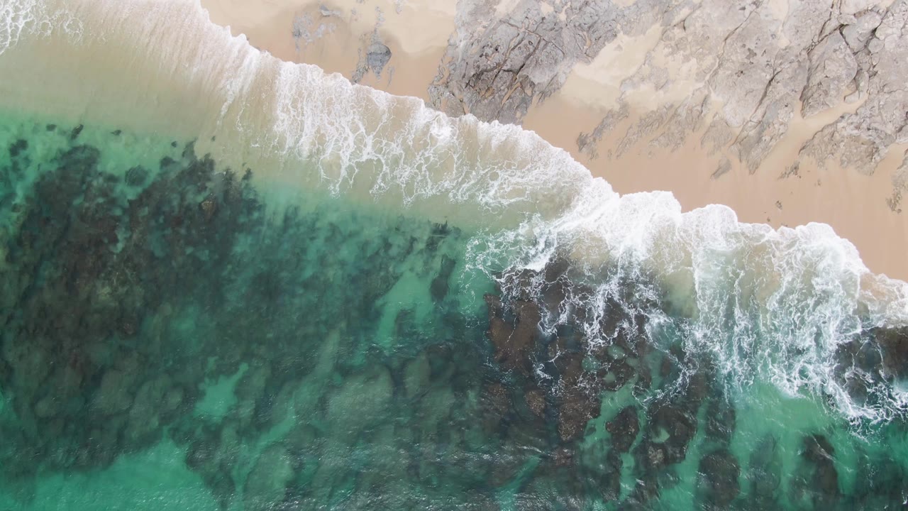 Overhead surf breaking over rocks beside pale sand
