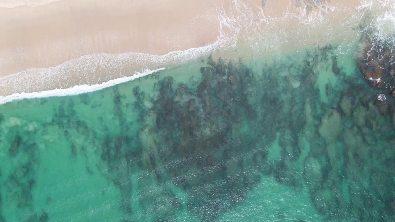 Overhead turquoise water and pale sand with white surf foam