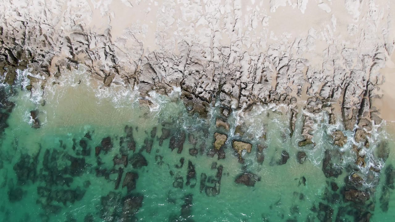Overhead view of turquoise water meeting rocky sand shoreline.