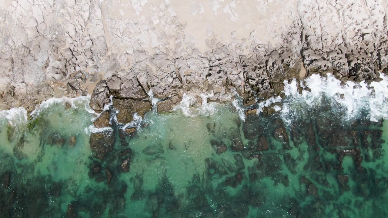 Rocky beach edge with receding foam over clear shallow water.