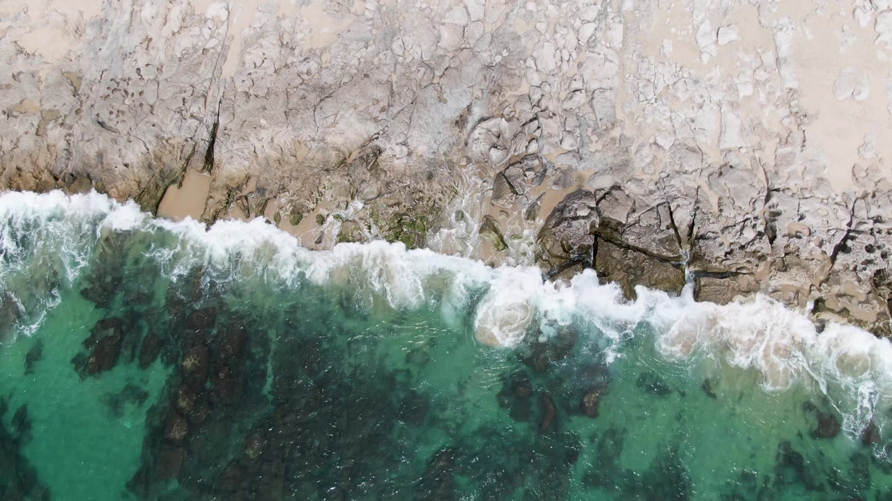 Overhead surf breaking along a pale rocky shoreline
