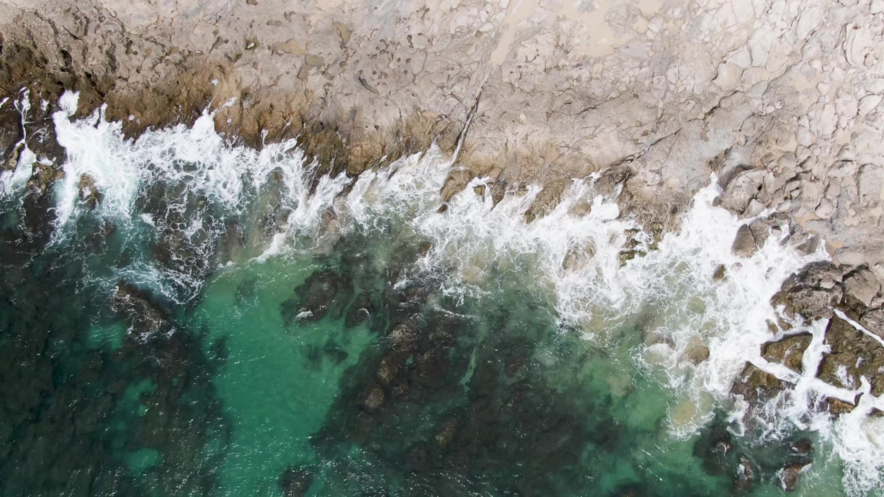 Overhead surf breaking against a pale rocky shoreline