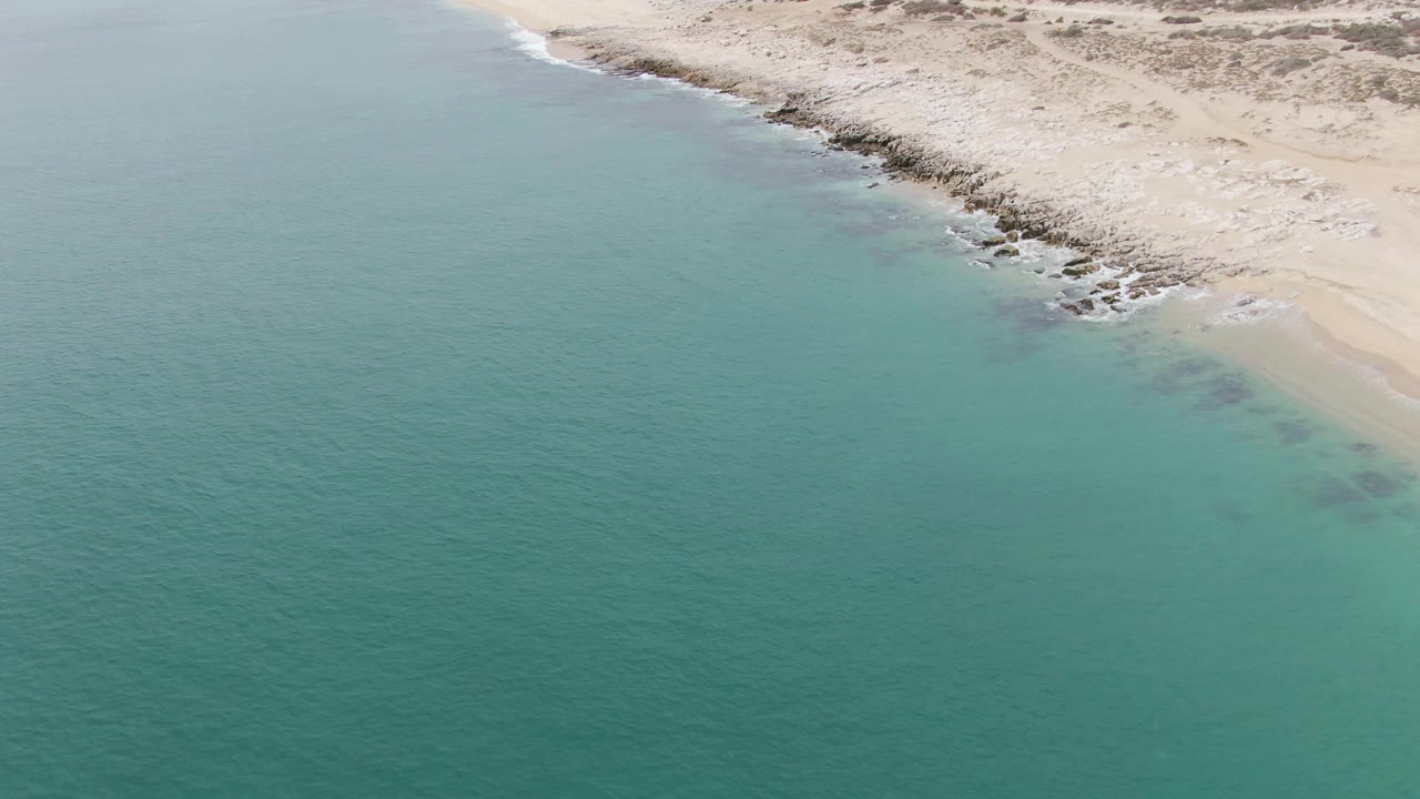 Open turquoise water below a sandy shoreline with small waves.