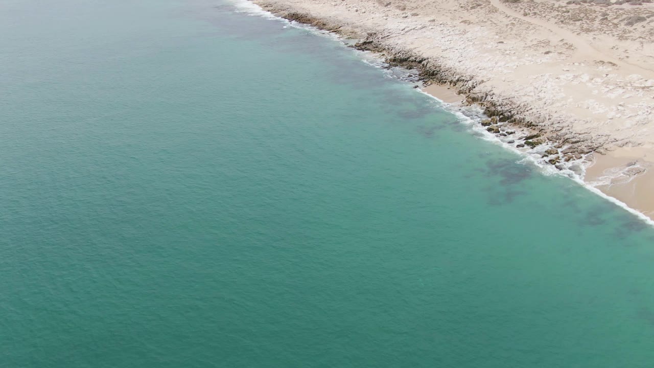 Aerial view of Punta Gorda Beach in Baja California Sur with turquoise water meeting a pale sandy and rocky shore, no visible people.