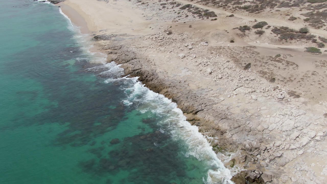 Oblique aerial view of surf washing onto a rocky beach edge