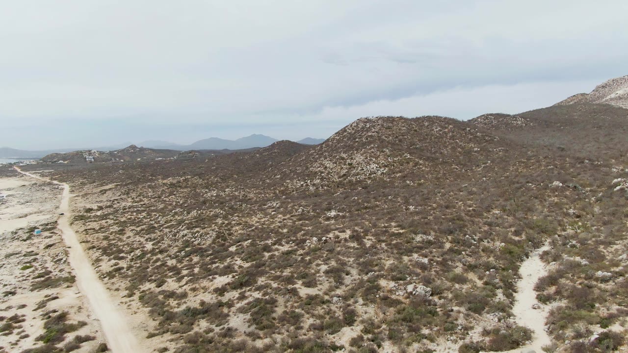 At 0:01, the Punta Gorda Beach aerial view centers more of the scrub-covered slope, with the dirt road running up from the lower left and no visible people.