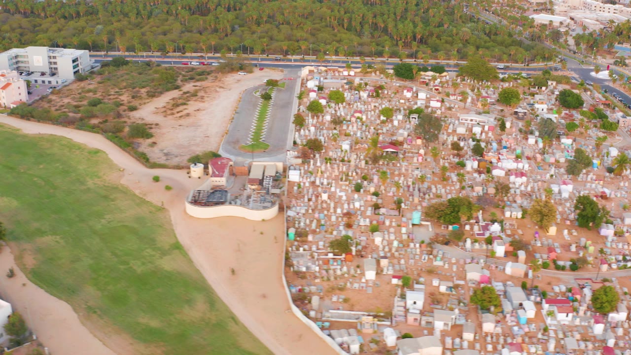 Aerial angle with green field in the foreground and dense structures to the right.