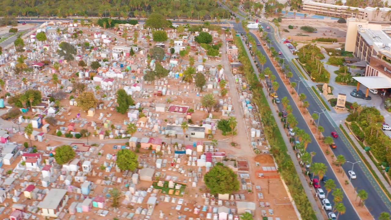 Overhead cemetery view with rows of graves and a road along the right edge.