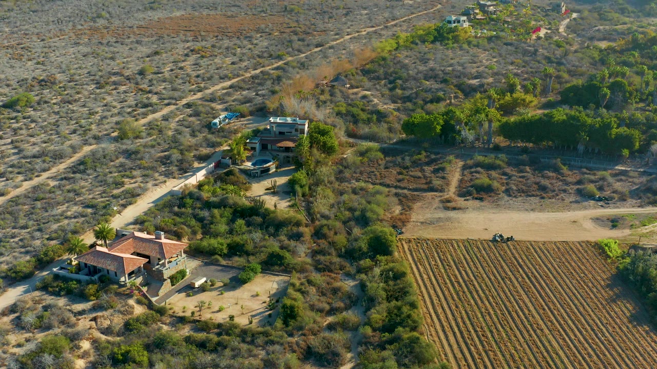 Aerial frame of a red-roof house, dirt road, brush, and farmland