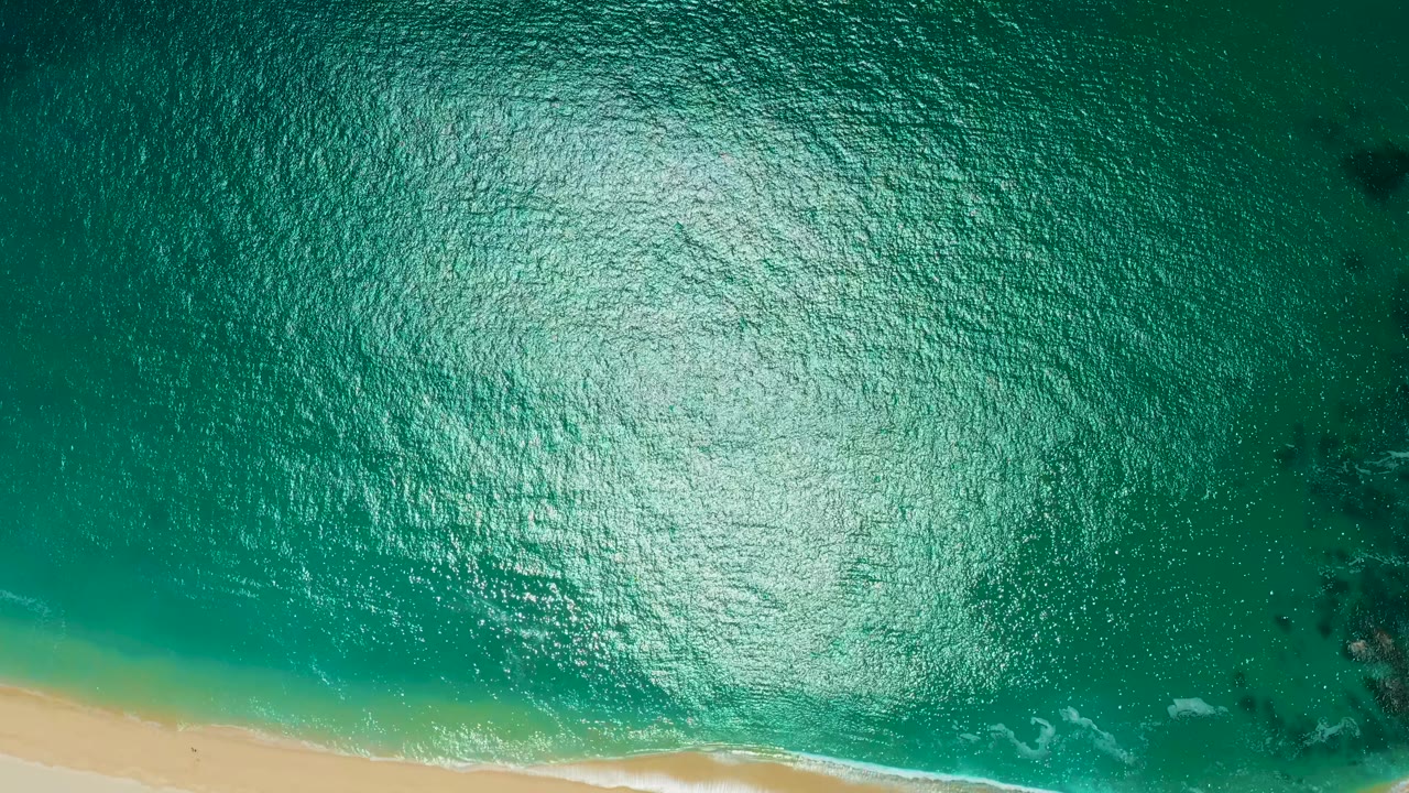 Overhead view at Marquis Los Cabos, Mexico showing turquoise ocean, bright water glare, a narrow sandy beach edge, and no visible people.