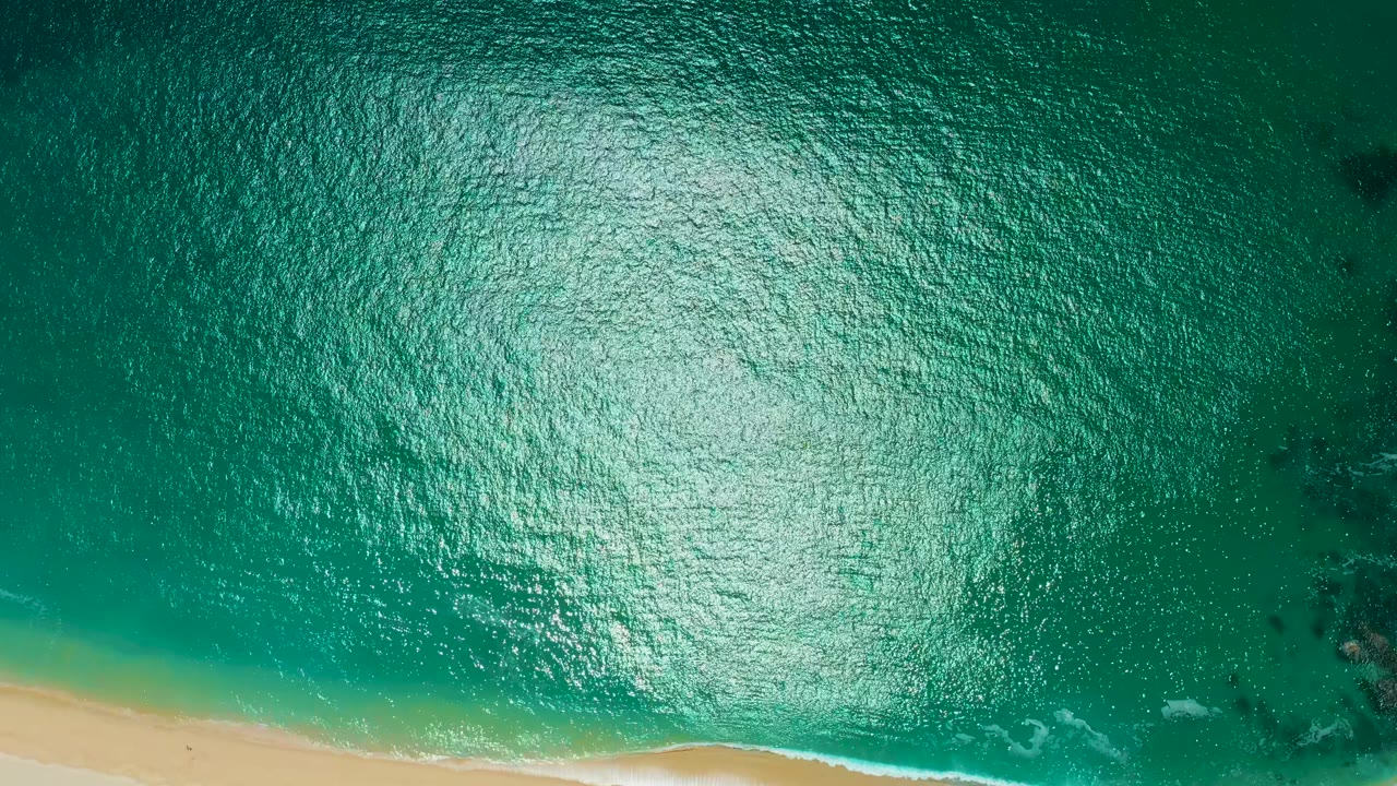 Overhead frame from Marquis Los Cabos, Mexico with sunlit turquoise water, the beach running along the lower edge, and no visible people.