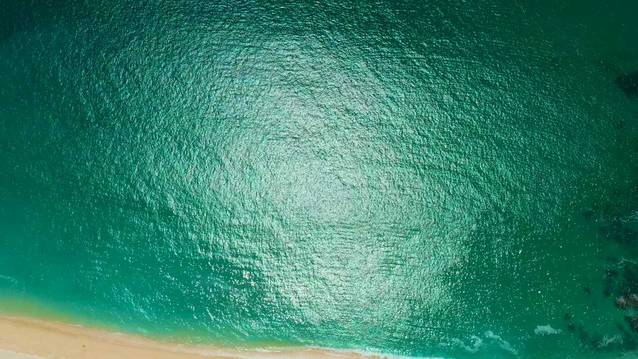 Bright overhead ocean surface beside a sandy beach