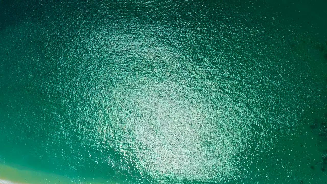 Aerial water surface at Marquis Los Cabos, Mexico, with the reflected light centered lower in frame and no visible people.