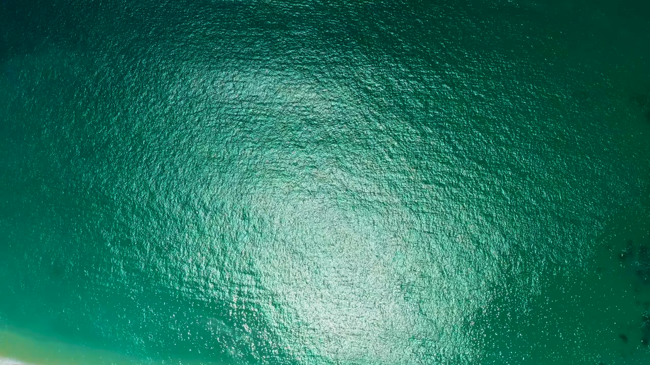 High aerial view of rippled teal water at Marquis Los Cabos, Mexico, with bright glare across the lower middle and no visible people.