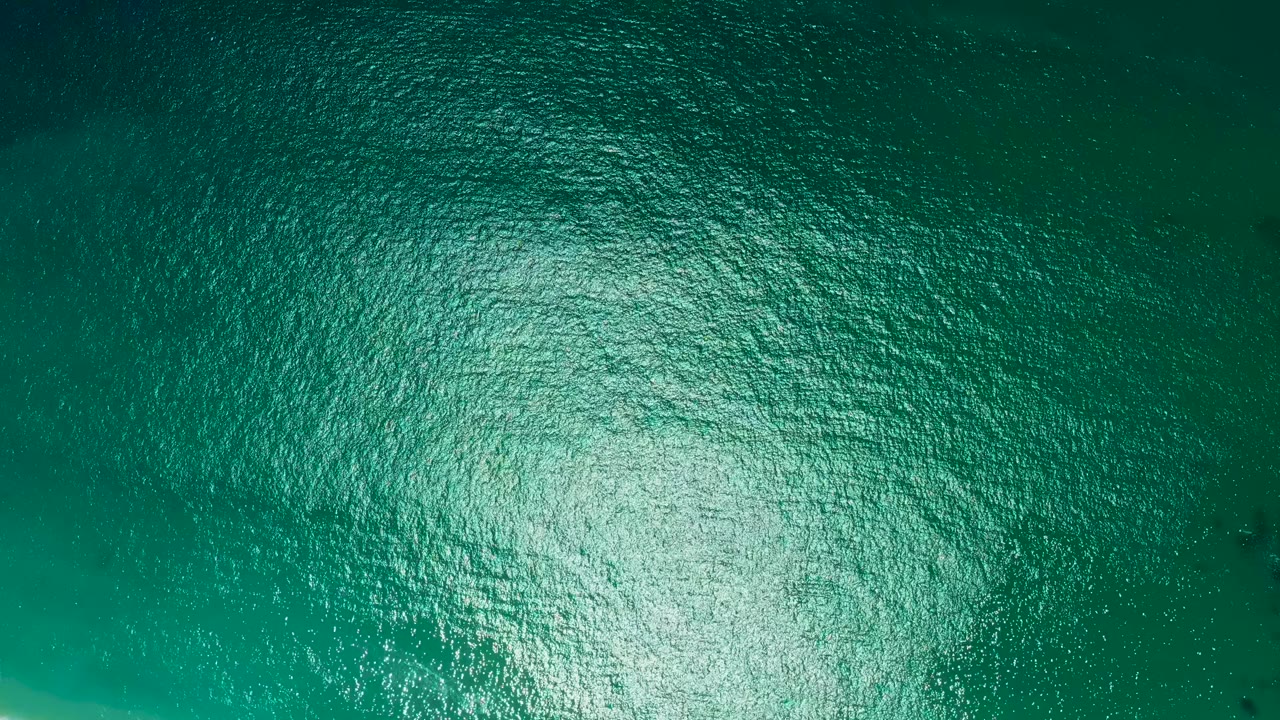 Overhead view of turquoise ocean water at Marquis Los Cabos, Mexico, with a broad bright sun reflection across small ripples and no visible people.